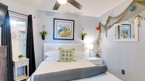 Un dormitorio con cama, mesita de noche, ventilador de techo y una obra de arte en la pared.