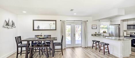A modern kitchen with a central island, dark wooden dining table, and chairs.