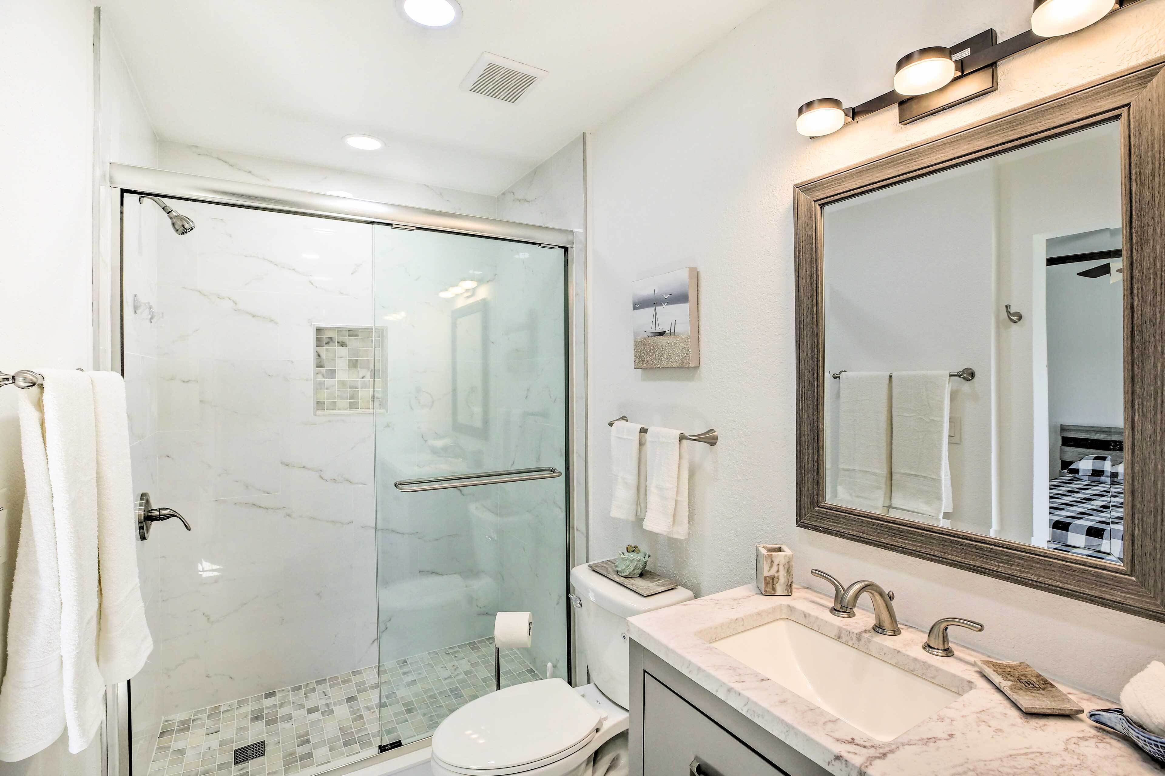 Une salle de bain moderne avec une douche à parois de verre, un grand miroir et un lavabo en marbre.