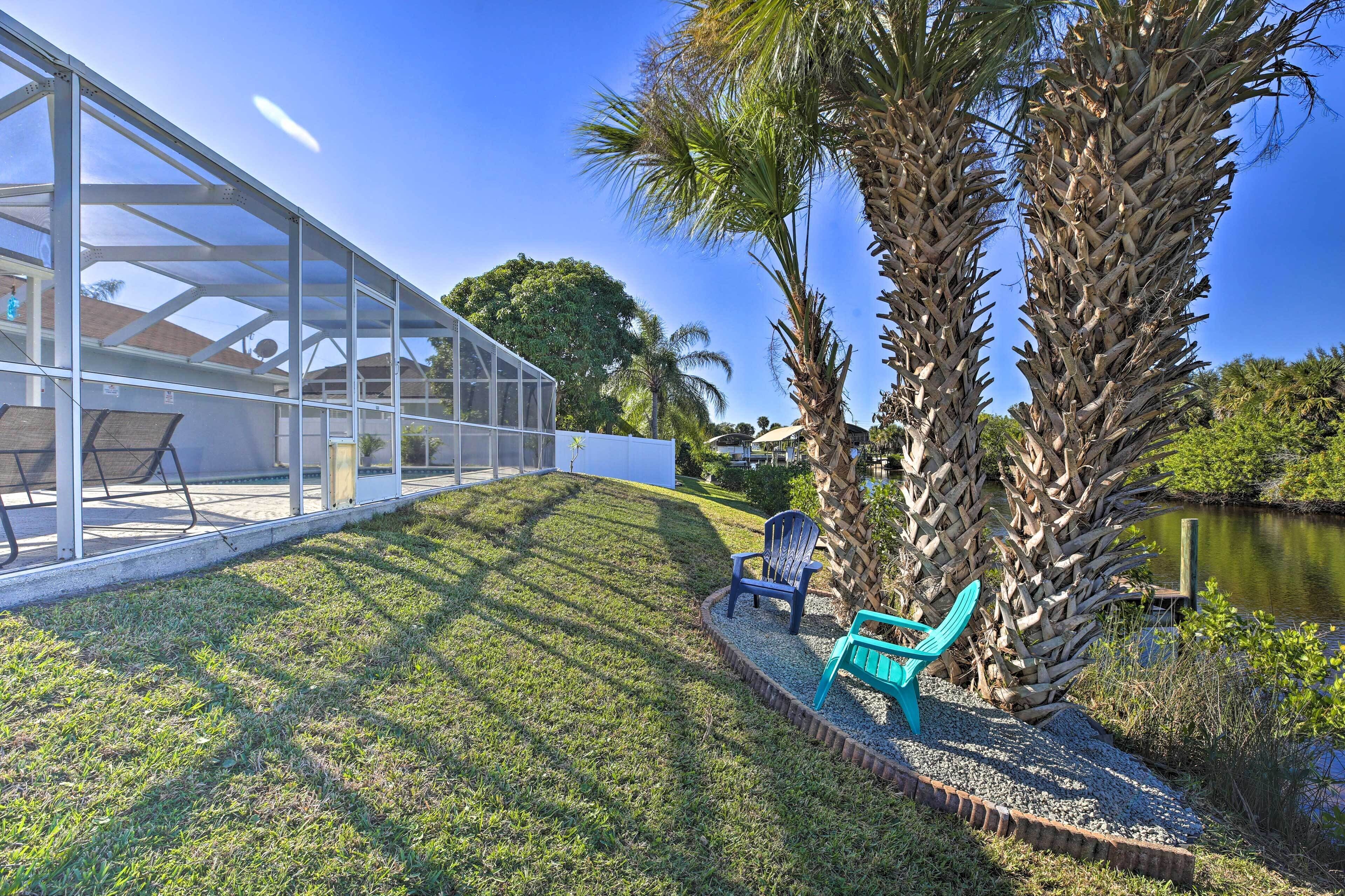 A modern house with a glass conservatory, a patio with chairs, and a pond.