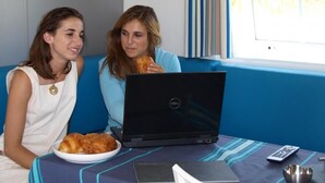 Twee personen zitten op een blauwe bank met een laptop, een bord eten en een afstandsbediening op een tafel.
