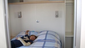 Een kamer met een bed, een plank boven het bed en een kledingkast.