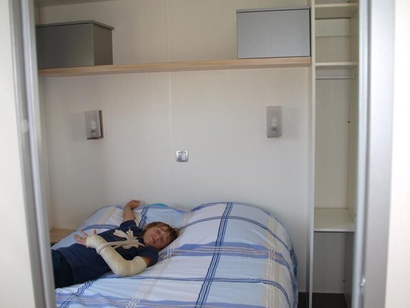 A room with a bed, a shelf above the bed, and a wardrobe.