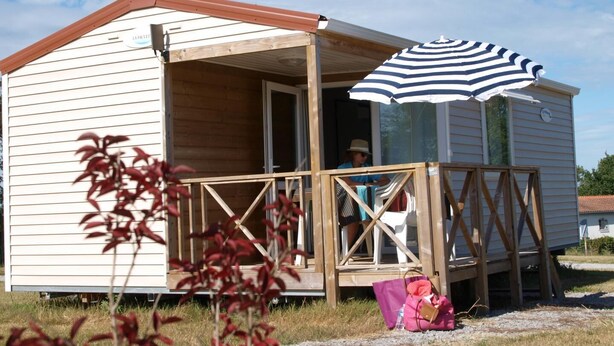 Een klein houten vakantiehuisje met een veranda en een strepen paraplu.