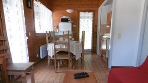 A cozy cabin interior with wooden walls, a dining area with a table and chairs, a kitchen with a microwave, and a red sofa.