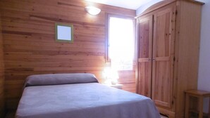 A bedroom with a bed, a wooden wardrobe, a small bedside table, and a window with curtains.