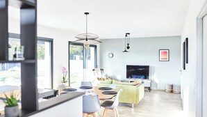 Ein modernes Wohnzimmer mit Essbereich, großen Fenstern und einem Fernseher.