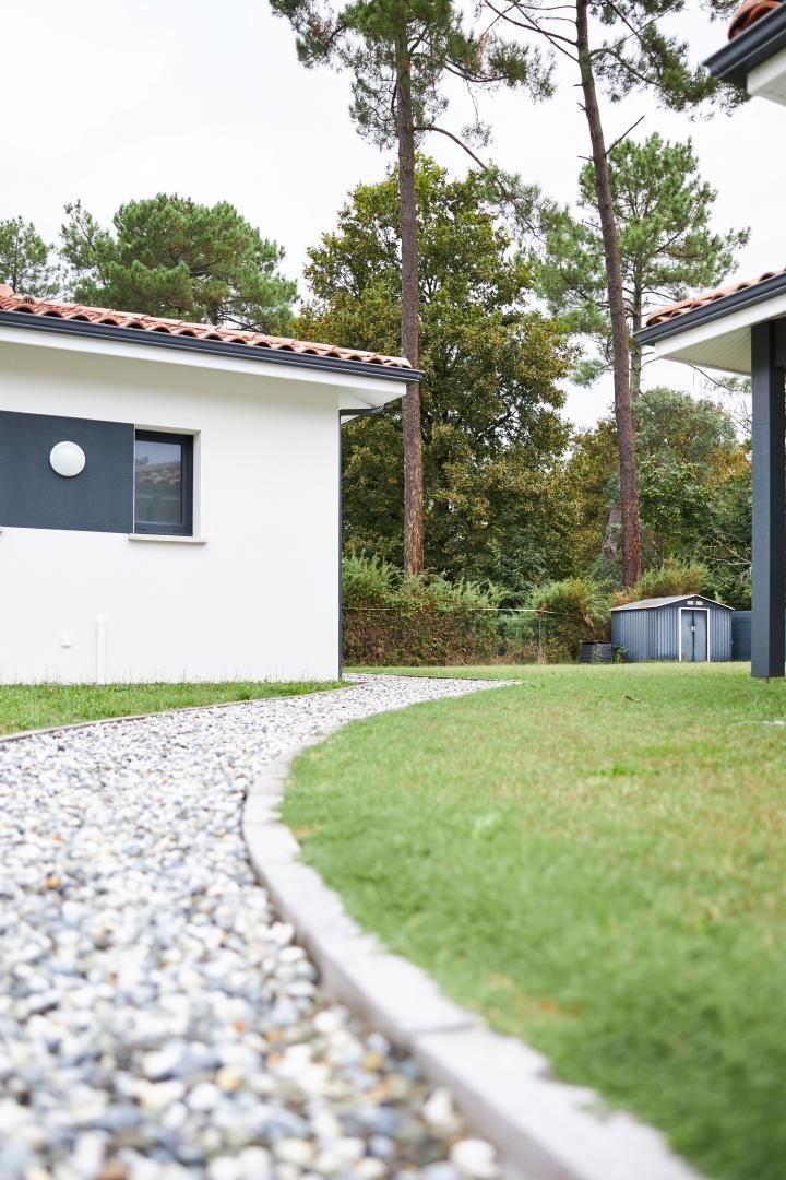 A modern building with a white exterior and a gravel pathway leading to a grassy area.