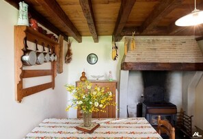 Traditional kitchen with a brick fireplace, wooden ceiling, and a wooden shelf holding kitchen utensils and pots.