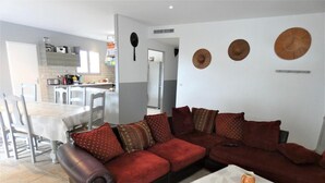 A living room with a brown sectional sofa, a white coffee table, and a dining area with a white table and chairs.