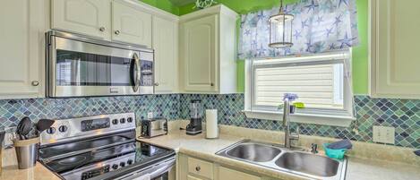 A kitchen with a stainless steel stove, oven, and microwave, a double sink, and a window with star-patterned curtains.