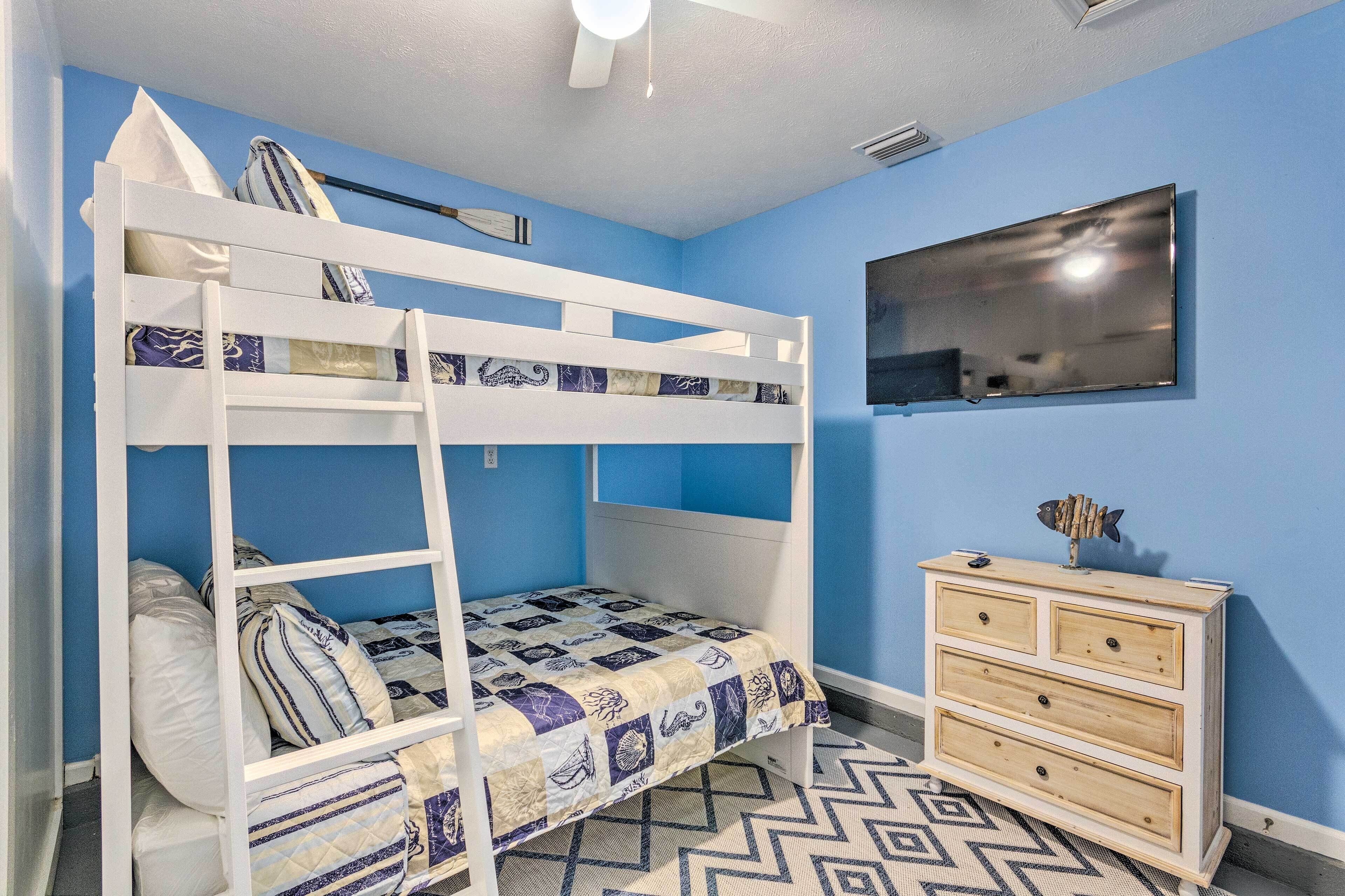 Una cama litera con colcha estampada, un aparador con cajones y un televisor de pantalla plana en la pared.