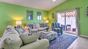 A living room with a green wall, a ceiling fan, a sofa, a coffee table, and a patterned rug. - PCB Retreat w/ Patio & Grill < 1 Mi to Beach! (Panama City Beach)