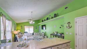 A kitchen with a green wall, a dining area with a table and chairs, and a white door. - PCB Retreat w/ Patio & Grill < 1 Mi to Beach! (Panama City Beach)