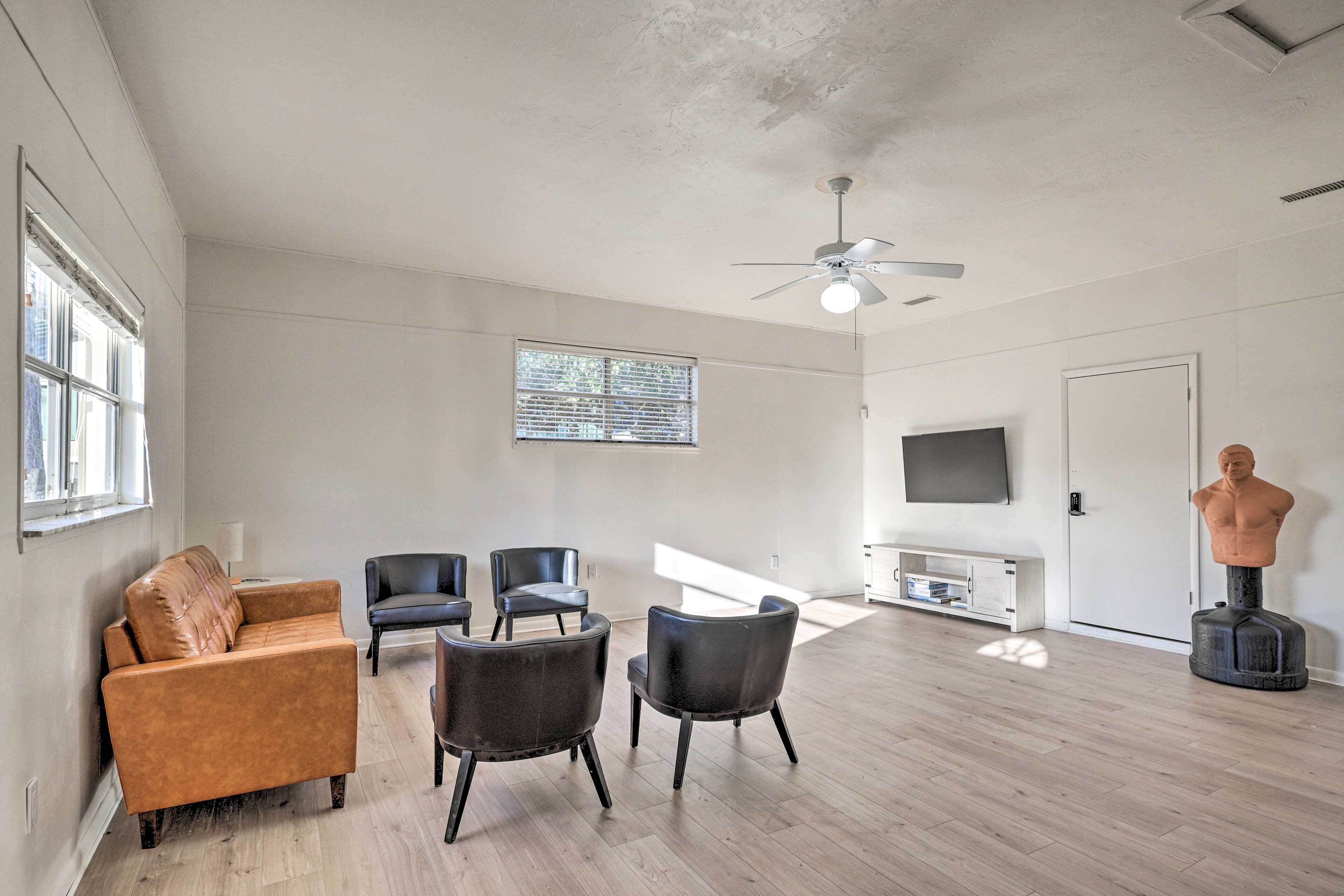 A spacious living room with a sofa, chairs, a ceiling fan, a TV, and a statue.