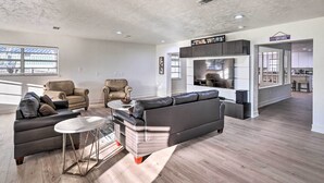 A spacious living room with a grey sectional sofa, a coffee table, and two armchairs. A kitchen area is visible in the background with a sign reading "Gators". - Spacious Family Home w/ Backyard in Gainesville! (Gainesville)