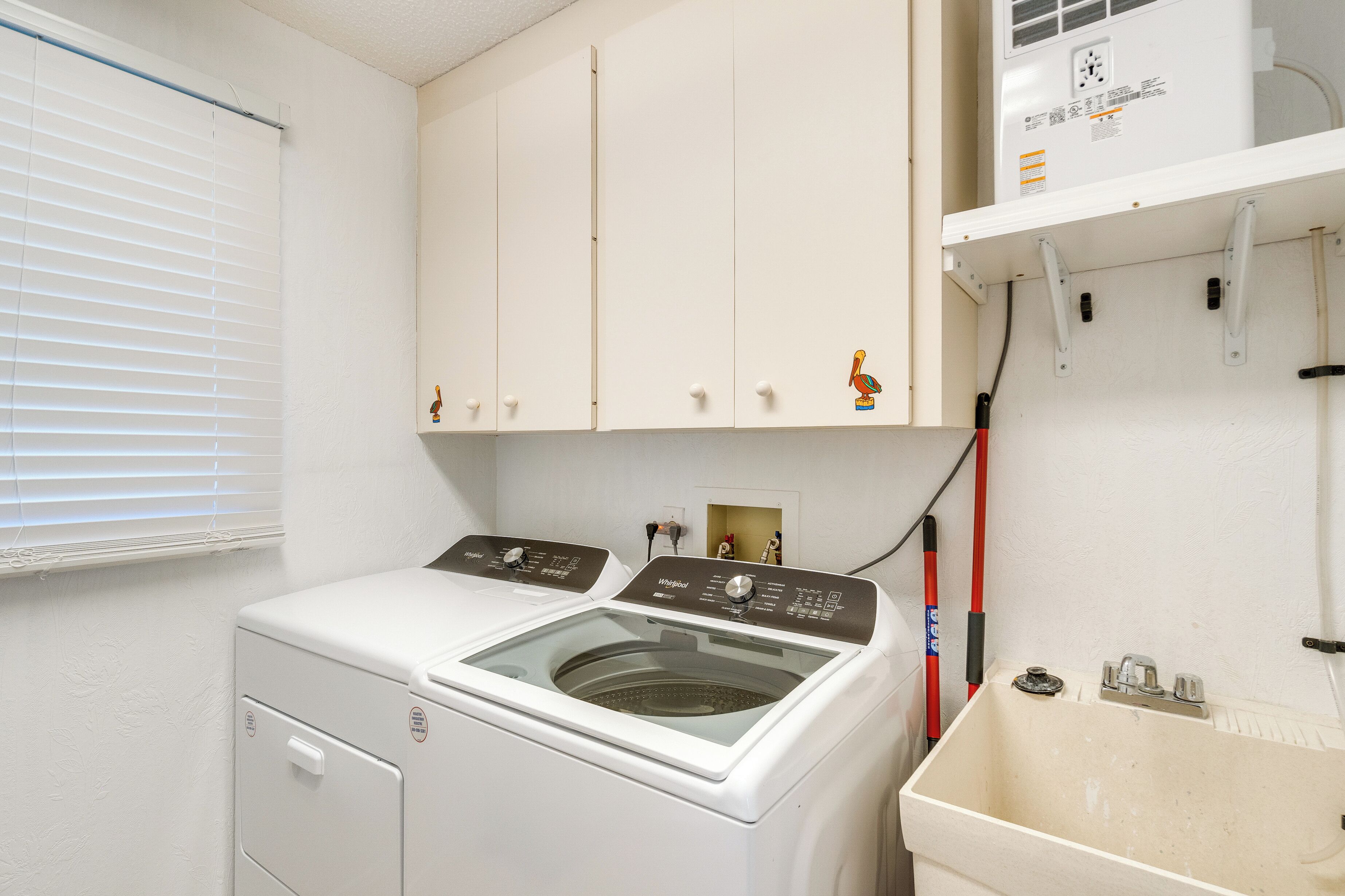 A laundry room with a front-loading washer and dryer, a utility sink, and a window with blinds.