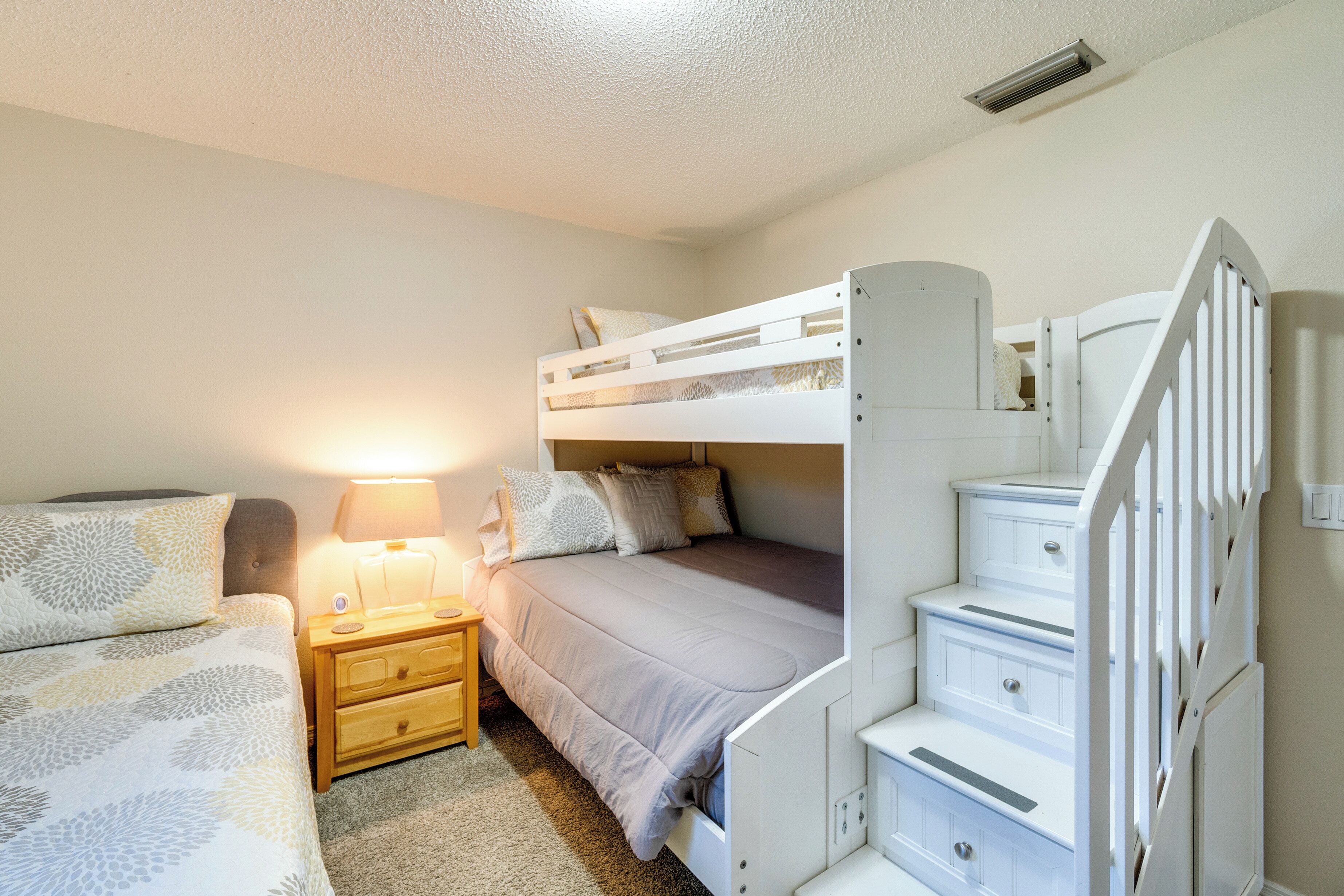 A bunk bed room with a nightstand and lamp, white walls, and a staircase.