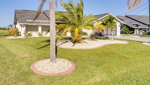 Una casa residenziale con un prato curato, palme e un vialetto in pietra.
