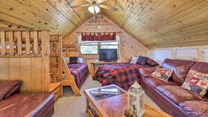 A cozy attic bedroom with wooden walls and a sloped ceiling, featuring two beds, a leather couch, and a television. - Hurley Lakefront Hideaway w/ Fire Pit & Dock! (Hurley)