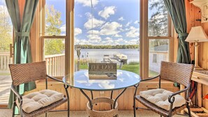 A cozy outdoor seating area with wicker chairs and cushions, a glass table, and a view of a lake with a sign reading "Welcome to the Lake." - Hurley Lakefront Hideaway w/ Fire Pit & Dock! (Hurley)