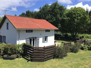 Een wit huis met een rood dak, een omheinde tuin en een bloemenpracht.