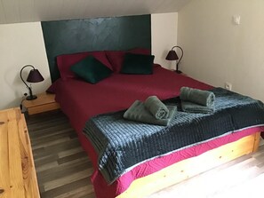 Een eenpersoonskamer met een rood sprei, twee groene kussens, een donkerblauwe deken en twee bedlampjes.