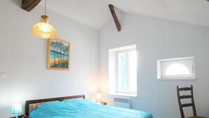 Een slaapkamer met een bed, een stoel, een raam, een schilderij en een hanglamp.