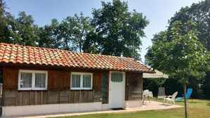 Et lille hus med et tag af teglsten, trævægge og en hvid dør. Der er en lille veranda med et bord og stole.