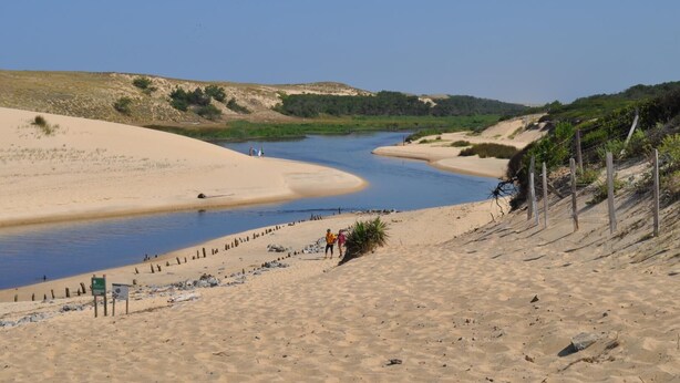 En sandstrand med en flod, et par personer og et hegn.