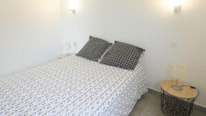 Et soveværelse med et mønstret sengetæppe, to puder, et natbord med en lampe og et lille rundt bord med en lampe.