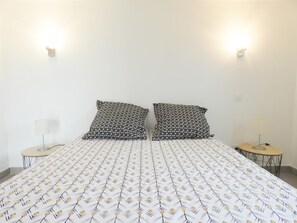 A bed with a patterned bedspread, two pillows, two bedside tables, and wall-mounted lights. - Pierron - Linxe - Gîte (LINXE)