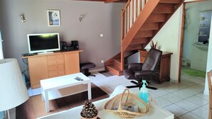 A living room with a TV, wooden staircase, and a dining area.