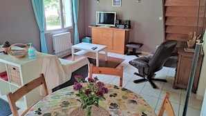 A cozy living room with a TV, wooden furniture, and a dining area with a table and chairs.