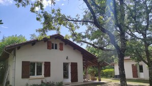 A two-story house with a covered patio, a small garden, and a tree in the foreground.