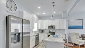 A modern kitchen with stainless steel appliances, white cabinets, and a bar area with stools. - 4 Blocks to Beach! Family-friendly Galveston Home (Galveston)