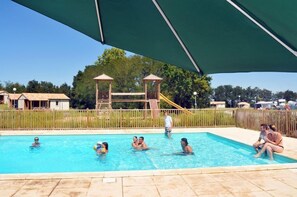 Uma piscina com pessoas na água, um parquinho infantil com um escorrega e uma área coberta com teto.