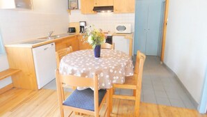 Une cuisine compacte avec des meubles en bois, une table à manger recouverte d’une nappe à motifs floraux et un petit réfrigérateur.