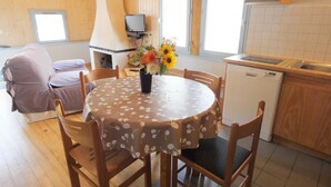 Une pièce chaleureuse avec une table ronde, des chaises en bois, un canapé, une cheminée, un téléviseur et un coin cuisine équipé d’un lave-vaisselle.
