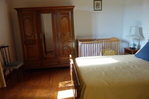 Cozy bedroom with a bed, crib, and nightstand, featuring a wardrobe and framed artwork.