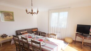 A dining area with a table set for four, a sofa, a TV stand, and a chandelier. - La Tanière - St-martin-de-seignanx (ST-MARTIN-DE-SEIGNANX)
