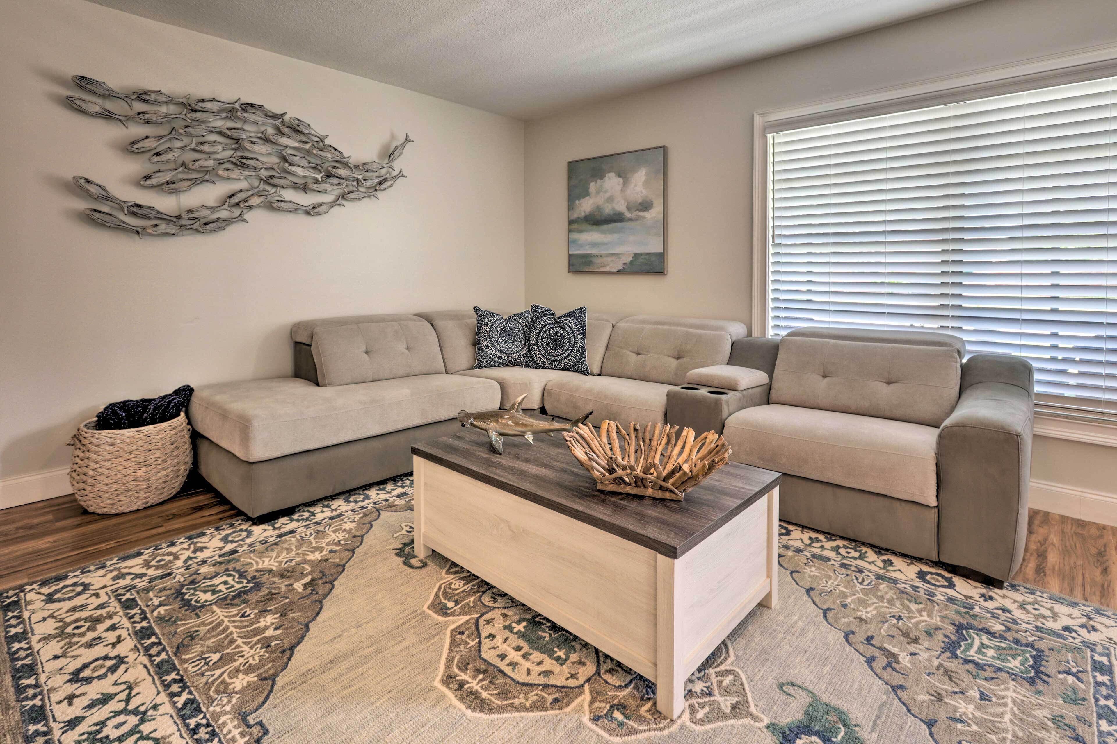 A living room with a beige sectional sofa, a wooden coffee table, and a patterned rug.