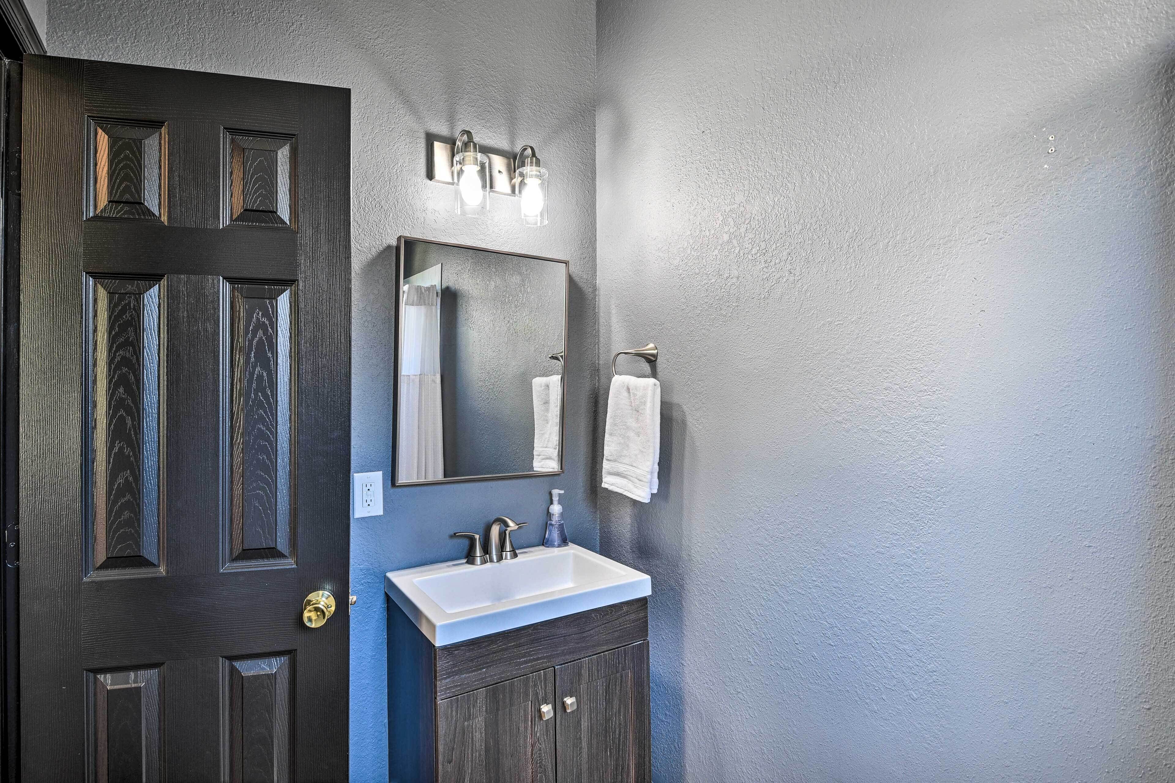 Un baño con una puerta de madera oscura, un lavamanos blanco y un espejo encima.