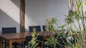 An outdoor dining area with a wooden table and chairs, surrounded by tall grasses and plants.