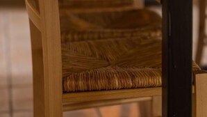 A wooden dining table with a woven chair in front.