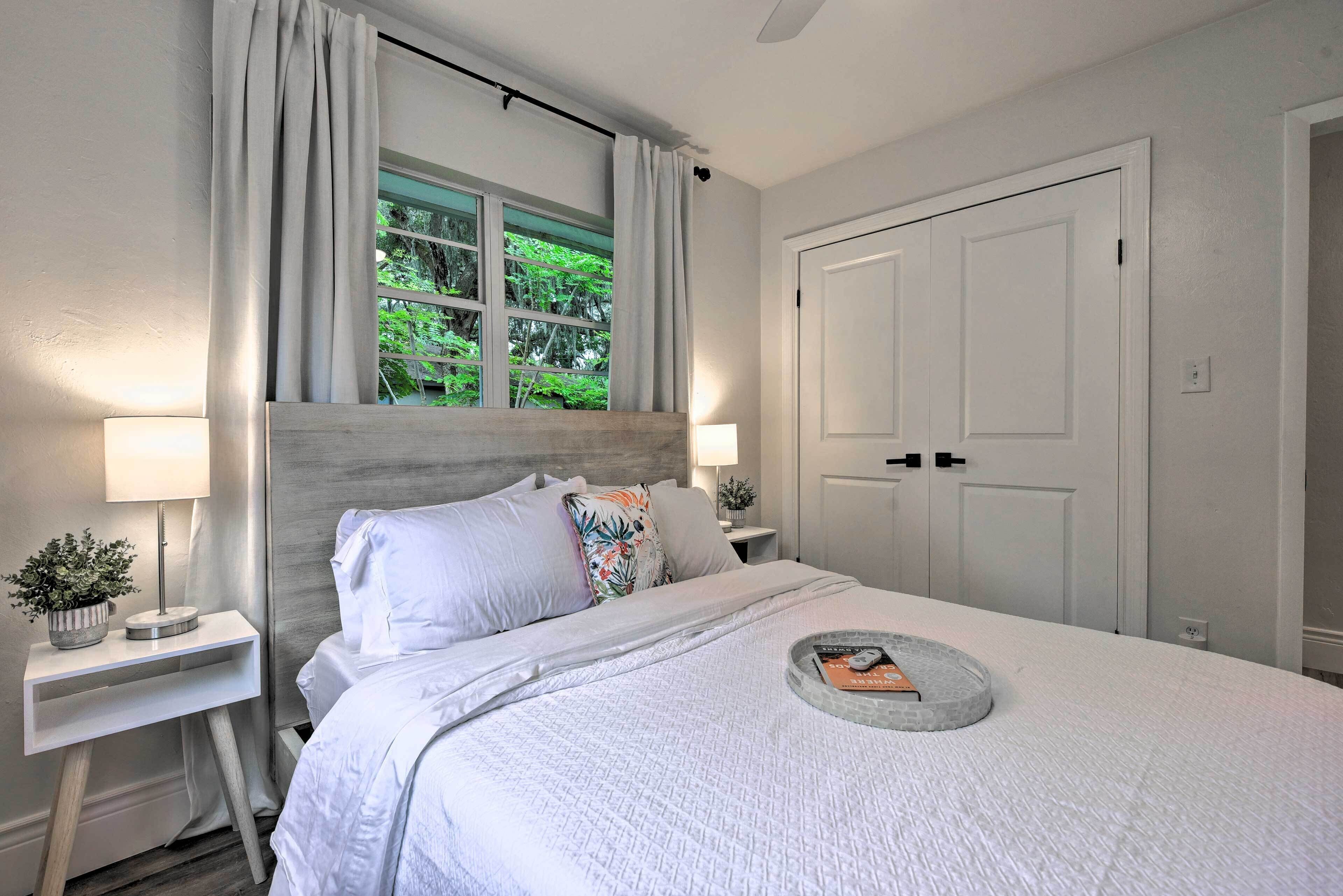A neatly arranged bedroom with a bed, bedside tables, a window with curtains, and a door.
