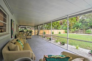 A covered patio area with beige sofas and a view of a backyard with a wooden fence and greenery.