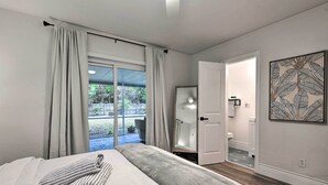 A bedroom with a bed, curtains, a bathroom with a toilet, and a view of the outside.