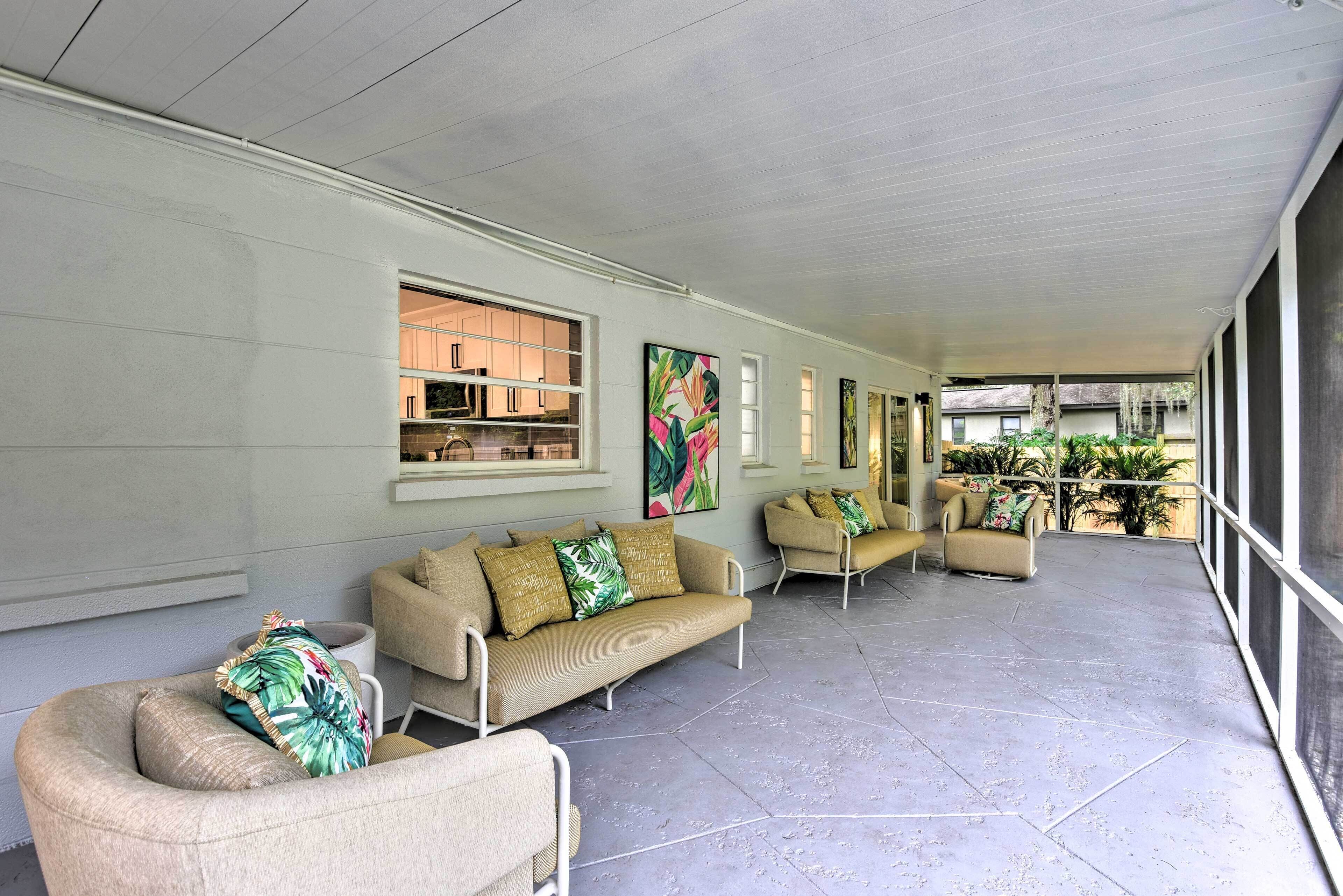 A covered outdoor seating area with beige sofas and chairs, large windows, and artwork on the walls.
