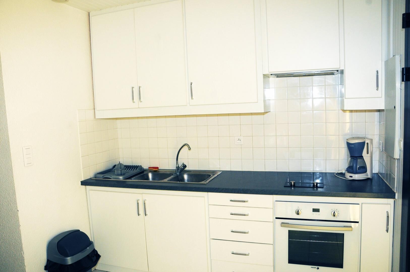 A kitchen with white cabinets, a double sink, a coffee maker, and a built-in oven.
